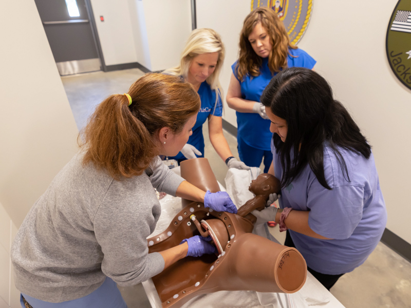 Maternal-fetal specialist Dr. Rachael Morris, left, demonstrates how to remove a newborn using a mannequin torso to AirCare base supervisor Cori Bitner, Baptist Hospital Jackson ER nurse Merrell Hourguettes; and Lifecare EMS paramedic Mayra Sanchez.