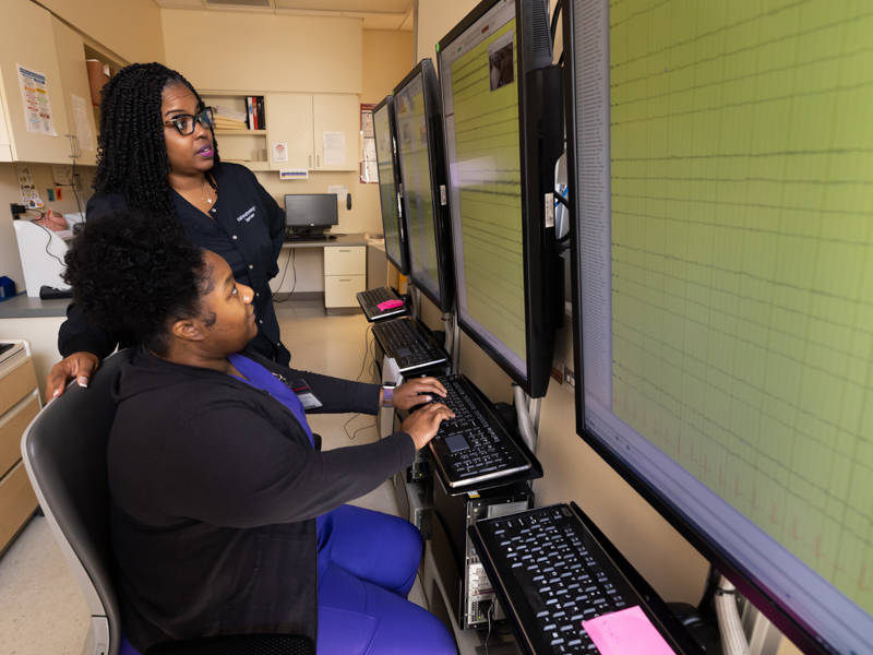 Skyla Wilson, standing, neurophysiology laboratory supervisor in the Department of Neurology, and Yvette McClendon, a neurodiagnostic assistant, study the real-time EEGs of patients in the Epilepsy Monitoring Unit.