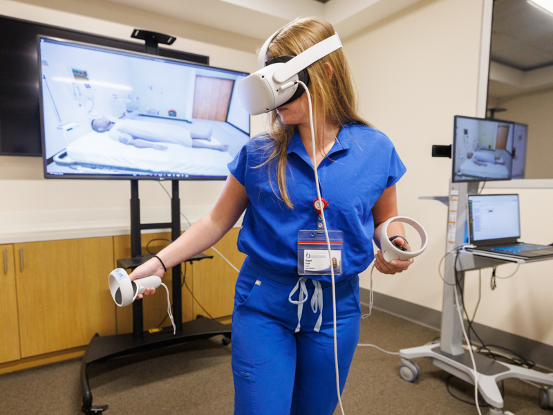 After donning a VR headset, second-year medical student Chappel Pettit uses hand controls to manipulate the features of a SimGym clinic.