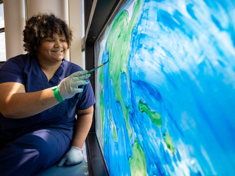 Makayla Bailey, a first-year nursing student, paints the finishing touches on North America on a window in a play room at Children's of Mississippi. Bailey volunteers weekly at the facility with patients and their families.