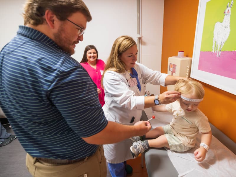 Dr. Kristin Weaver measures patient William Harreld as dad Daniel Harreld offers him a treat. Looking on is mom Christy Harreld.