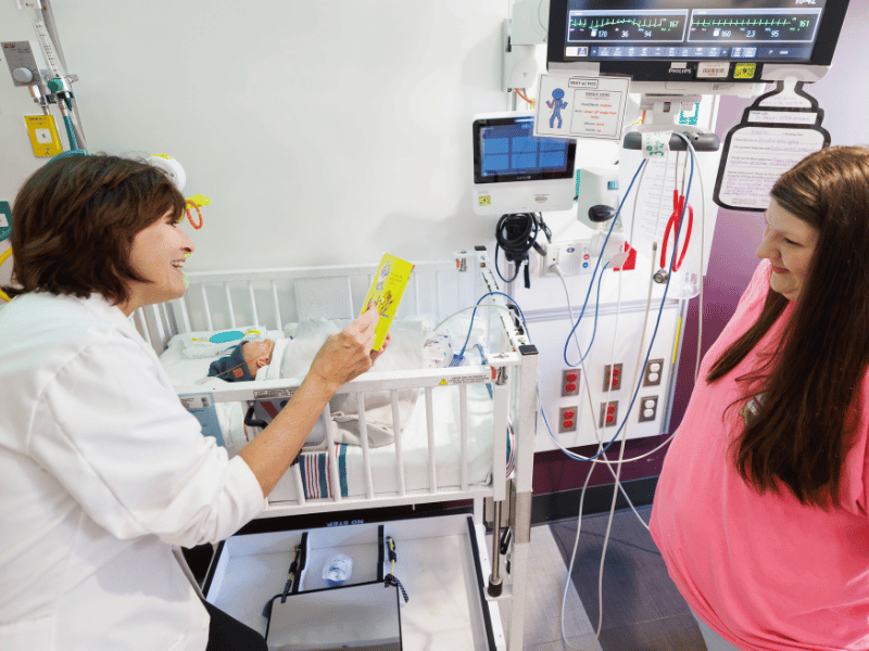 Dr. Mary Taylor, Suzan B. Thames Chair and professor of pediatrics, joins in the NICU Read-a-thon at Children's of Mississippi by reading "Giraffes Can't Dance" to Waylon Teague of Collinsville as his mom, Hannah Teague, looks on. Melanie Thortis/ UMMC Communications