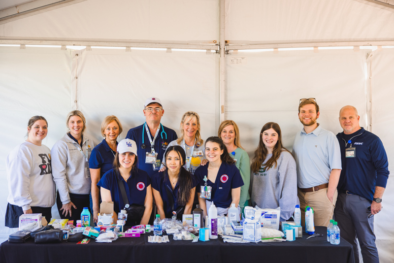 group of nurses and nursing students manning a first aid tent at a golf championship. The group is standing behind a table full of first aid and medical supplies