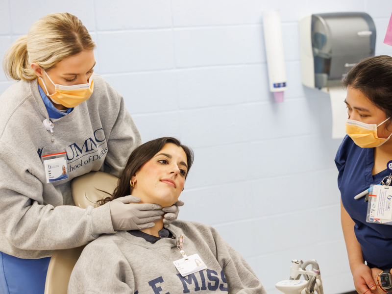 Nursing student, Junnah Mondejar, watches as dental hygiene students, Anna Shaw [left] and Mary Gillespie, demonstrate how to conduct an oral cancer screening.