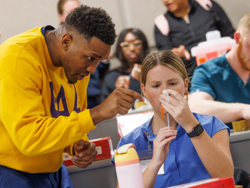 Nursing student Shelton Cole shows dental hygiene student, Morgan Kaminski, how to extract from a vile.