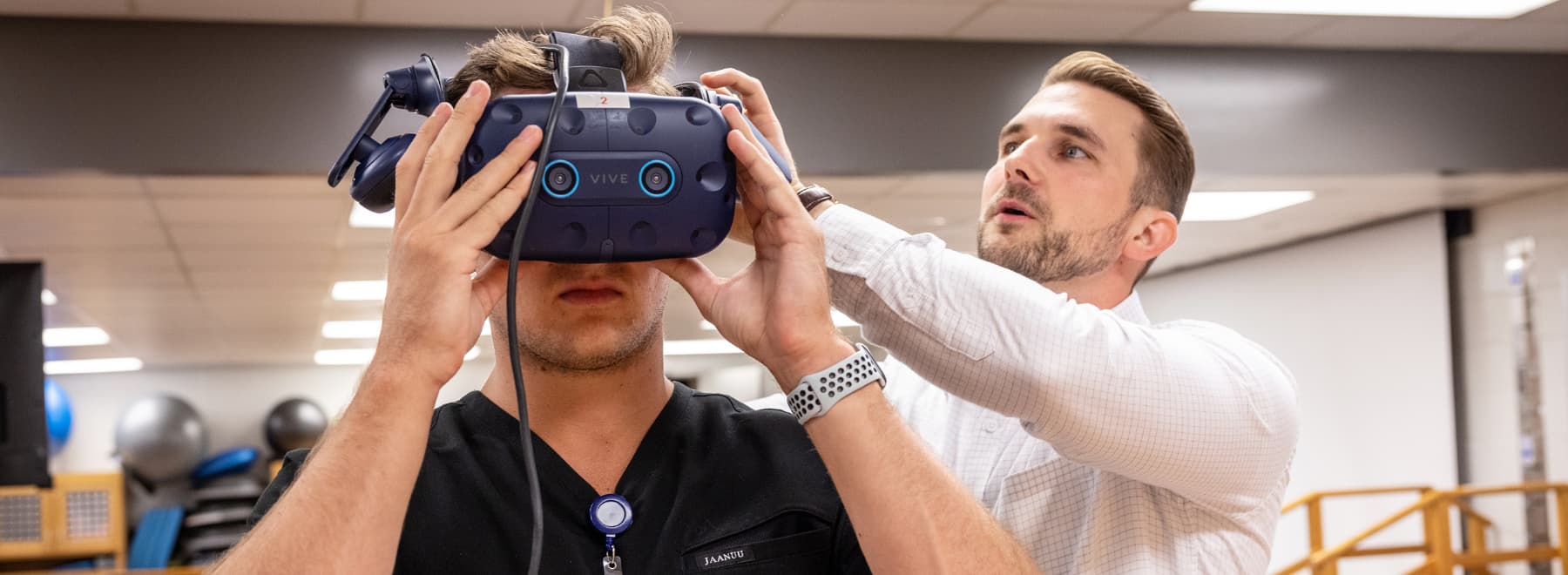 Dr. Jacob Daniels assists PT student Jacob Lape, of Jackson, in fitting a VR headset used to help study neurological reactions in concussion studies.