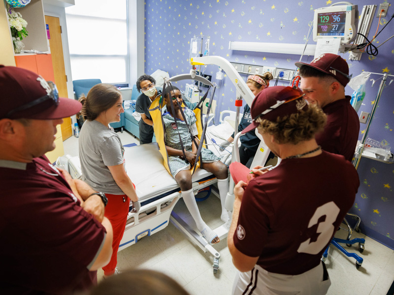 Willie Brooks, of Greenville, a patient at Children's of Mississippi, is visited by MSU head coach Chris Lemonis and players David Mershon and Nate Chester. They are joined by occupational therapists Martha Mims Rodgers and Lucy Alexander.