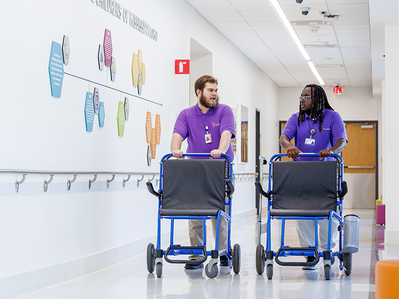 Neal Carpenter, left, and Creighton Johnson roll wheelchairs down a hallway at Children's of Mississippi during their internship with Ambassador Services at UMMC.