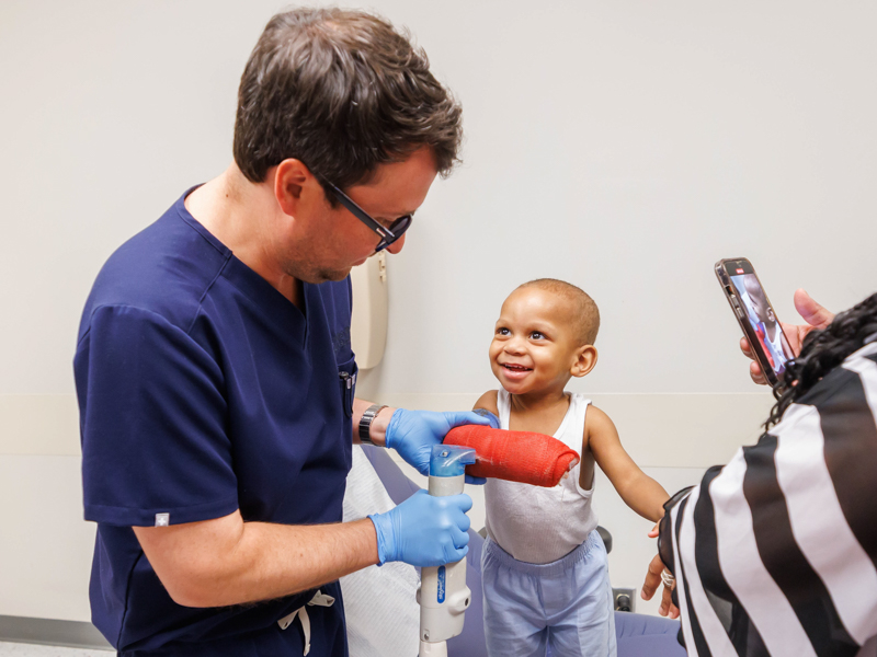 Kobe Abron smiles while Dr. Marc Walker cuts his cast off with a saw. Filming her laughing grandson is Stacey Hughes of Jackson.