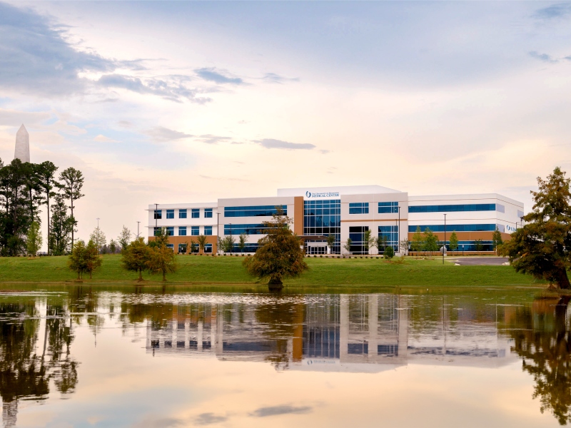 The University of Mississippi Medical Center Colony Park South features a large office building and a tranquil pond in front.