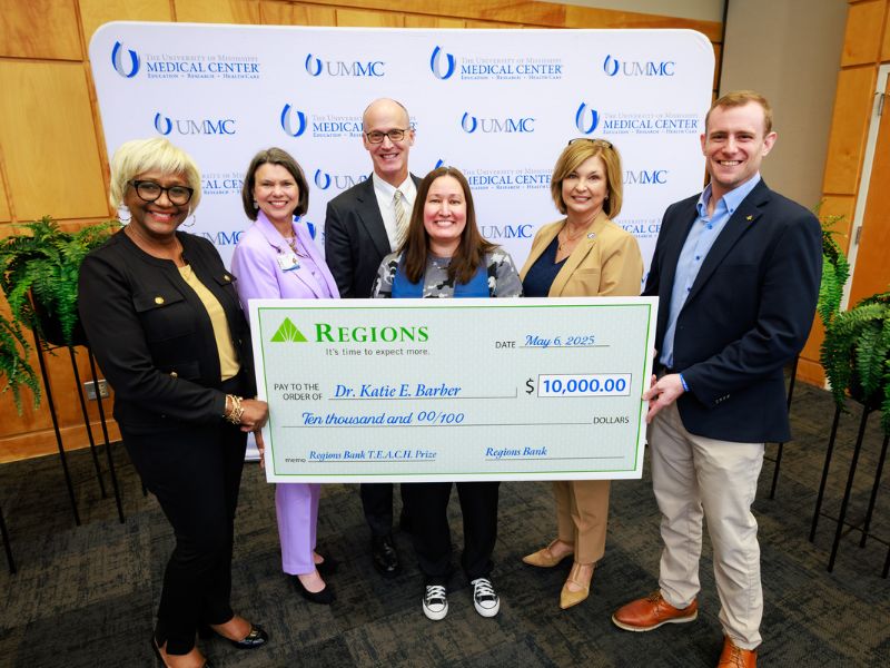 TEACH Prize honoree Dr. Katie Barber, center, receives congratulations and a $10,000 facsimile check from Regions Bank officials LoRose Moore, far left, and Myer Mack, far right. Between them are, from left, Dr. Donna Strum, dean of the School of Pharmacy; Dr. Scott Rodgers, associate vice chancellor for academic affairs; and Dr. LouAnn Woodward, vice chancellor for health affairs and dean of the School of Medicine.