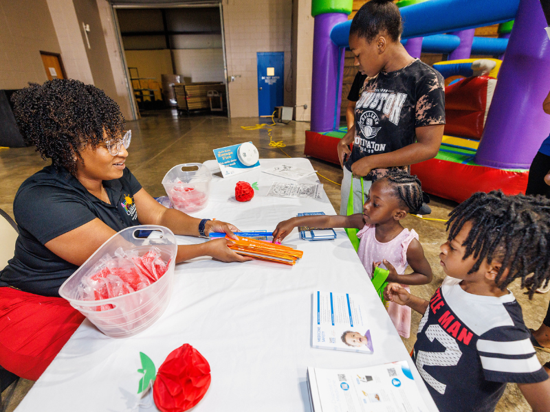 Liz Graves, project manager for Safe Kids Mississippi, offers school supplies to Kylie, Mikiyah and Mikel Johnson of Greenville.