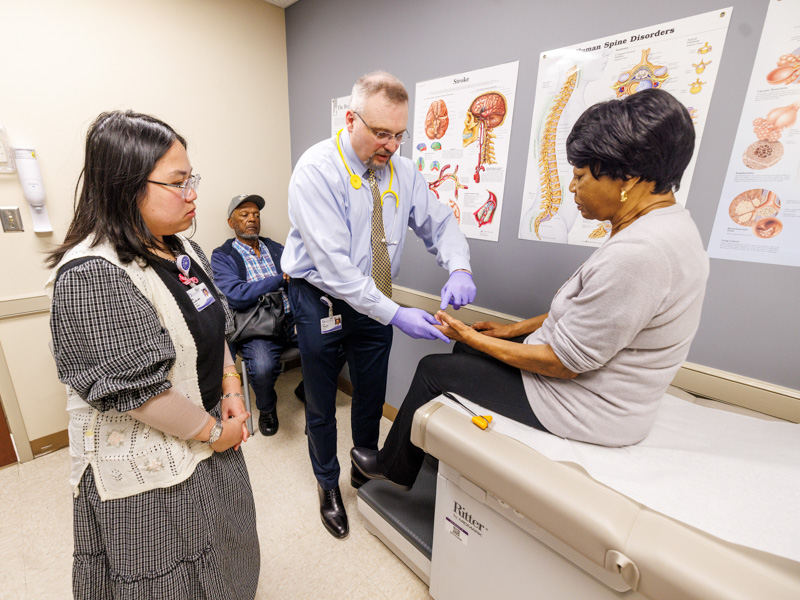 UMMC genetic counselor Phuc Do, left, observes as Dr. Pawel T. Pomianowski, the state’s only practicing adult geneticist, examines patient Louise Allen during a visit focused on research into the transthyretin gene variant. The hereditary condition disproportionately affects African Americans. Allen’s husband, Vincent Allen, attends in support.