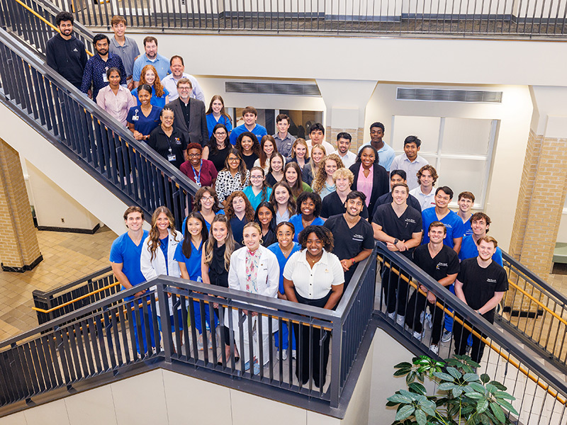 Group picture of UPSTART students and mentors standing at the intersection of two flights of stairs.