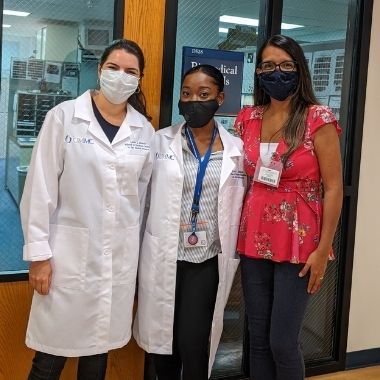 Three people stand in front of a door, two of them wearing their new white coats.