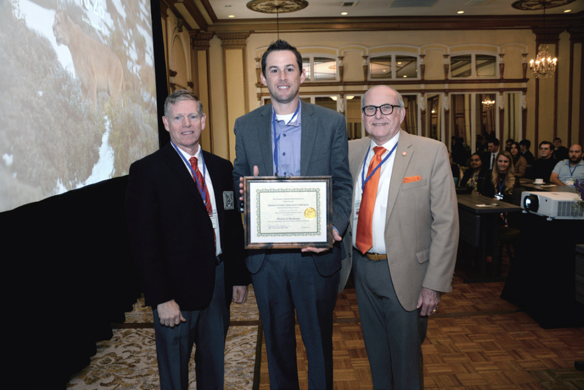 Michael Bierdeman poses with two gentleman while holding a certificate.