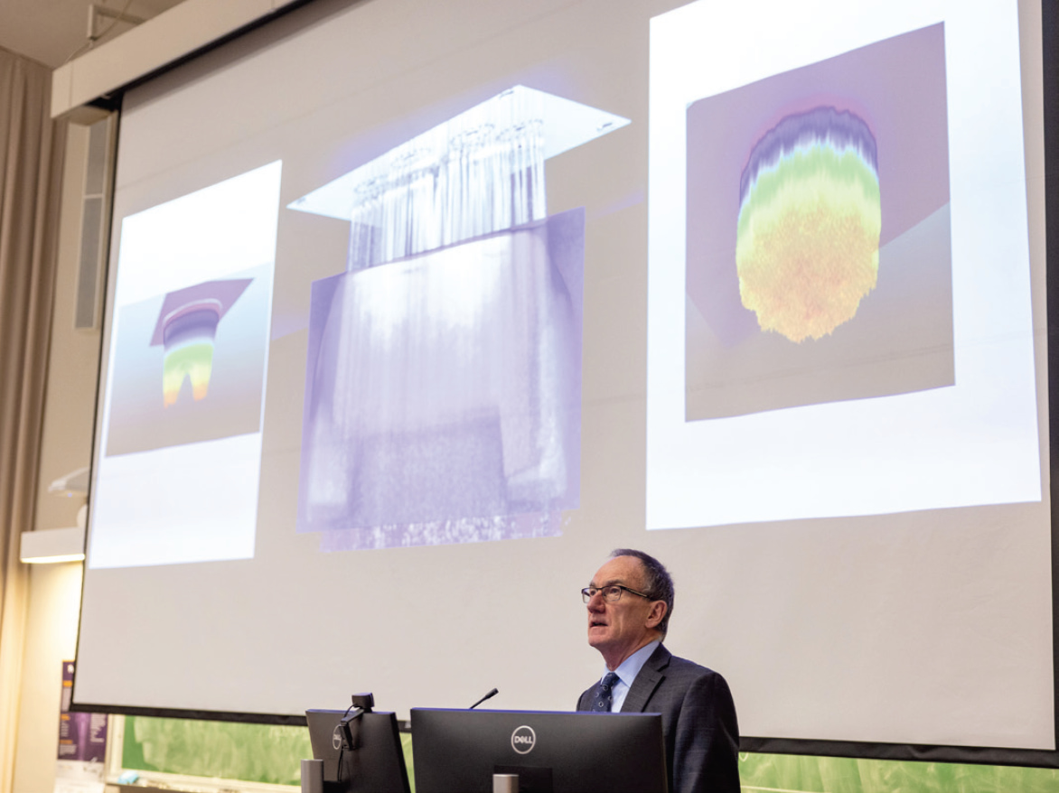 Dr. Richard Price speaking with an overhead projector bihind him displaying scientific illustrations.