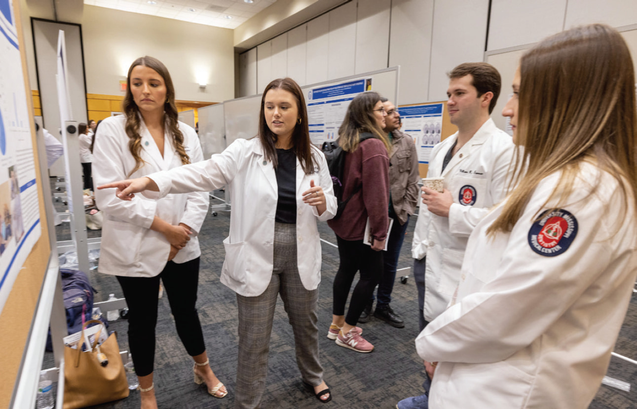 A student points out an item on a presentation poster as three other students look on.