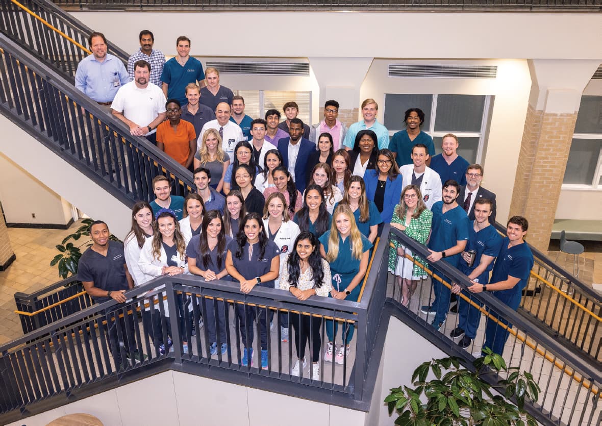 Indoor group shot 2023 UPSTART program participants with their faculty mentors stanning at the intersection of two flights of stairs.