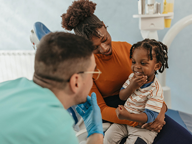 Smiling mother and child in the dentist's office as the child shows his teeth to the dentist.