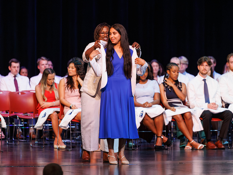 During an M1 White Coat Ceremony, Dr. Loretta Jackson-Williams joyfully assists a medical student with putting on her white coat.