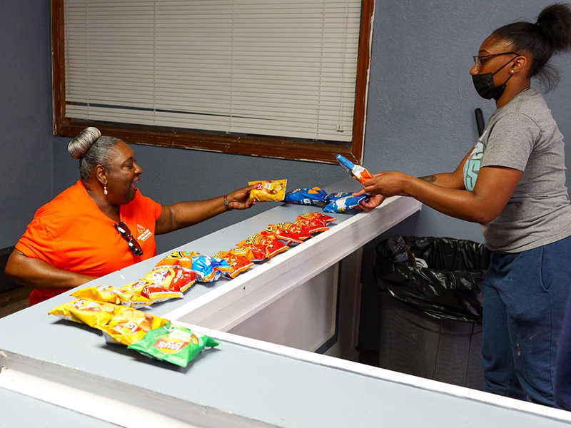 Two people, one seated, arranges free snacks on a counter.