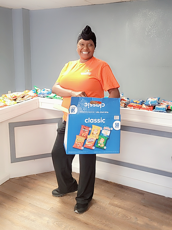 Event facilitator holding a box of assorted potato chips in front of a snack counter.