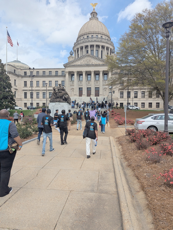 Group wearing matching shirts walking toward the Mississippi State Capitol during an organized advocacy march.