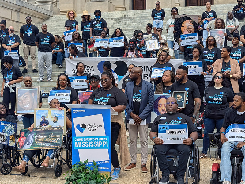 Large group gathered on Capitol steps holding survivor signs and memorial photos during a Crime Survivors Speak Mississippi rally.