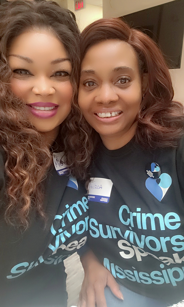 Two participants standing together indoors wearing Crime Survivors Speak Mississippi shirts and name badges.