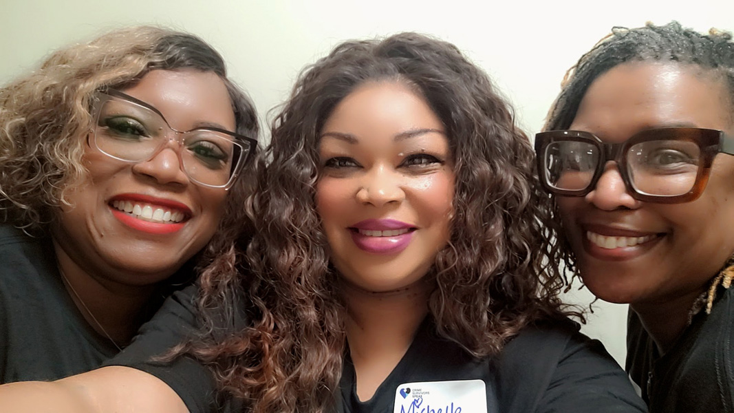 Three participants leaning together for a group photo indoors while wearing matching event shirts.