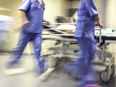 Action shot of two emergency room staff members pushing a gurney with a patient on it.