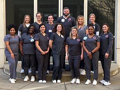 Group of thirteen nursing students standing in front of glass doors outside the School of Nursing building.