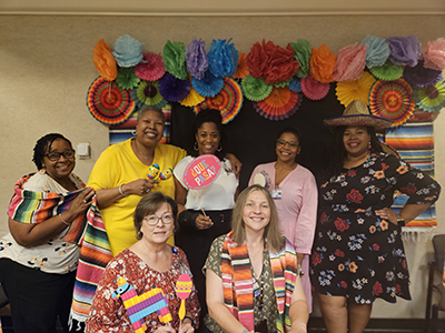 group of faculty and staff holding props standing in front of a Hispanic themed photo booth