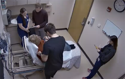 simulation scenario with a simulated patient on a hositpal bed being evaluated by nursing students